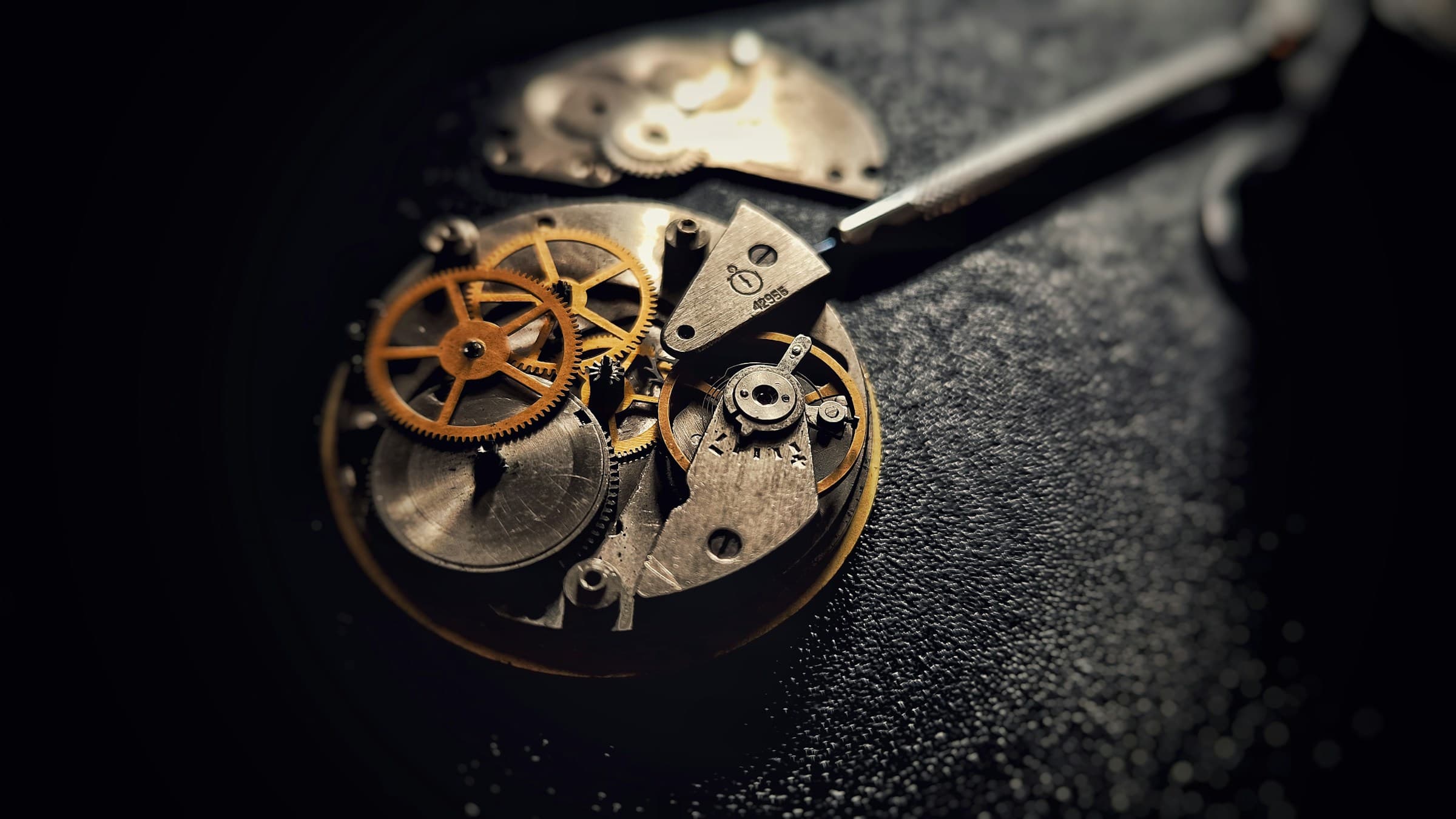 Close-up of a vintage watch movement with brass gears on a dark surface.